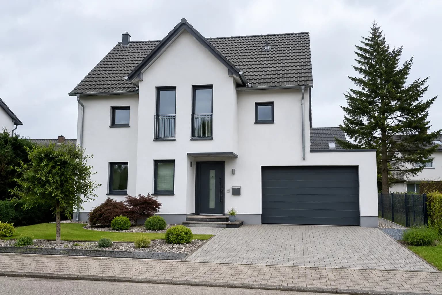Weißes Einfamilienhaus mit Satteldach, Garage und gepflasterter Einfahrt